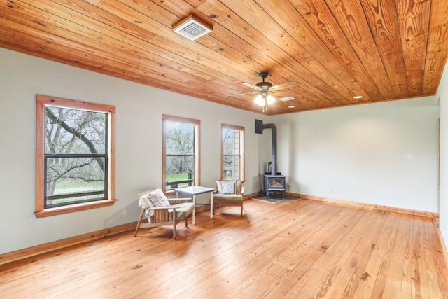 living area featuring a wood stove, wooden ceiling, ceiling fan, and light hardwood / wood-style flooring