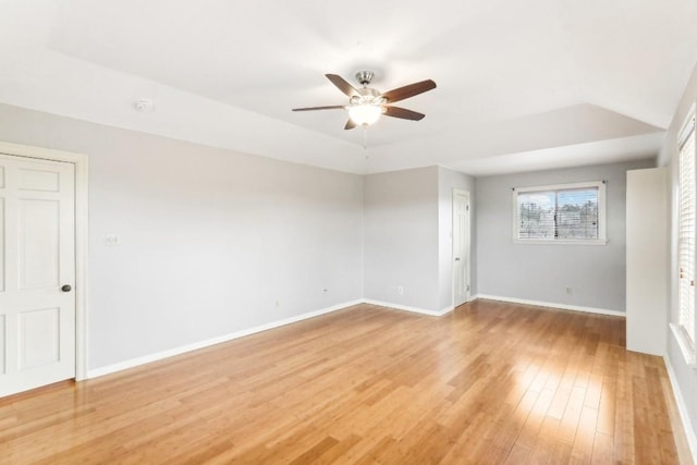 empty room with a tray ceiling, ceiling fan, and light hardwood / wood-style flooring