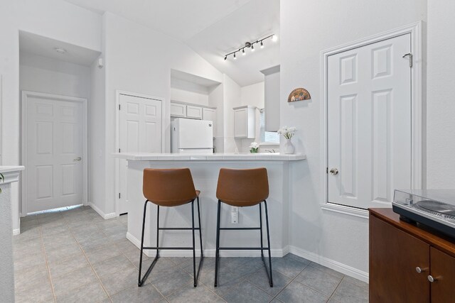 kitchen featuring white refrigerator, lofted ceiling, a kitchen bar, and light tile patterned flooring