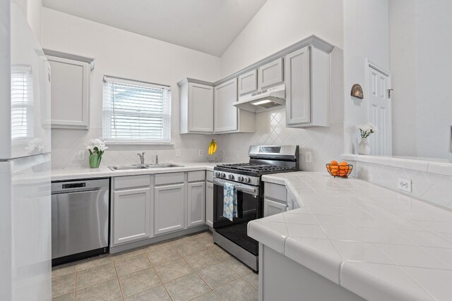 kitchen featuring sink, vaulted ceiling, backsplash, stainless steel appliances, and tile countertops