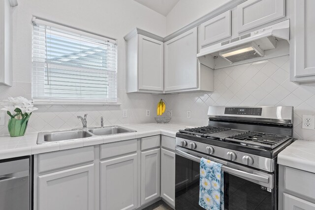 kitchen with appliances with stainless steel finishes, tile countertops, sink, and decorative backsplash