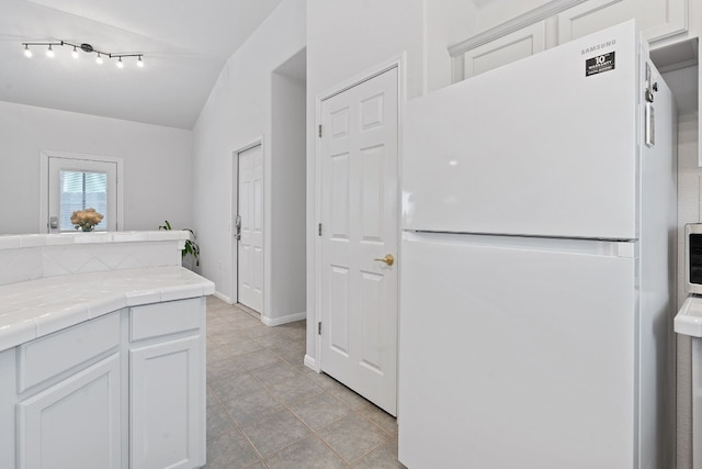 kitchen featuring vaulted ceiling, tile countertops, white cabinetry, white fridge, and light tile patterned floors