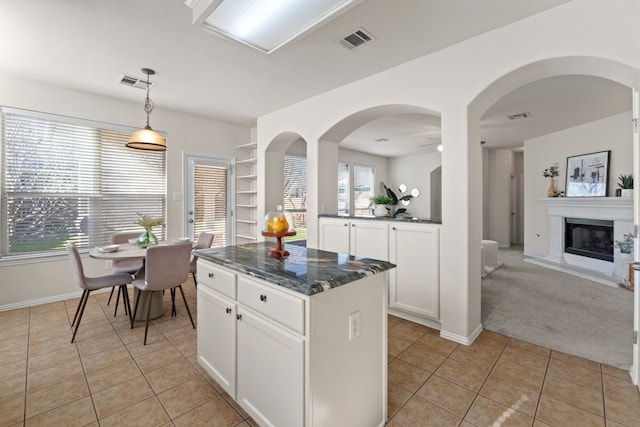 kitchen with light tile patterned floors, dark stone countertops, a center island, white cabinets, and decorative light fixtures