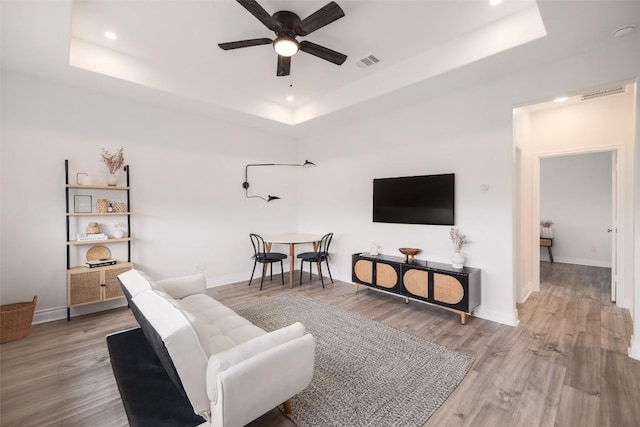 living room with light hardwood / wood-style flooring, a raised ceiling, and ceiling fan