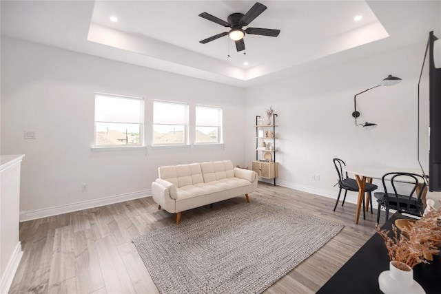 living room featuring light hardwood / wood-style floors, a raised ceiling, and ceiling fan