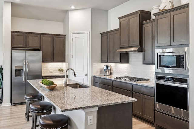 kitchen featuring a kitchen island with sink, sink, light stone counters, and stainless steel appliances