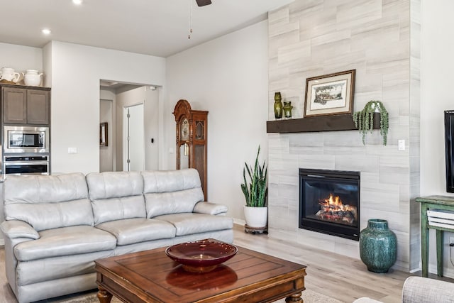 living room featuring a fireplace, ceiling fan, and light wood-type flooring