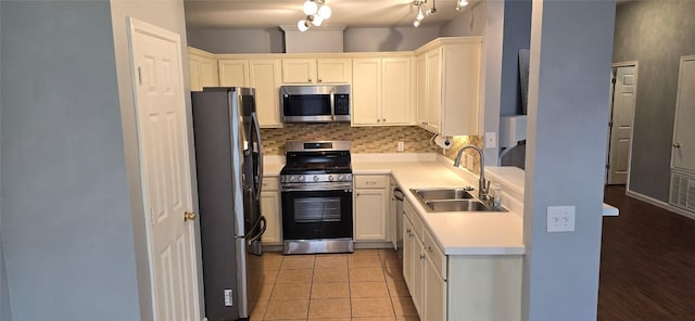 kitchen featuring sink, appliances with stainless steel finishes, white cabinets, light tile patterned flooring, and decorative backsplash