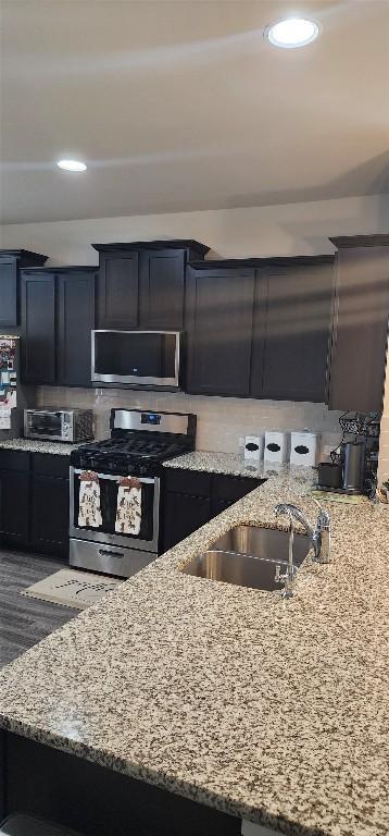 kitchen with stainless steel appliances, a sink, and light stone countertops