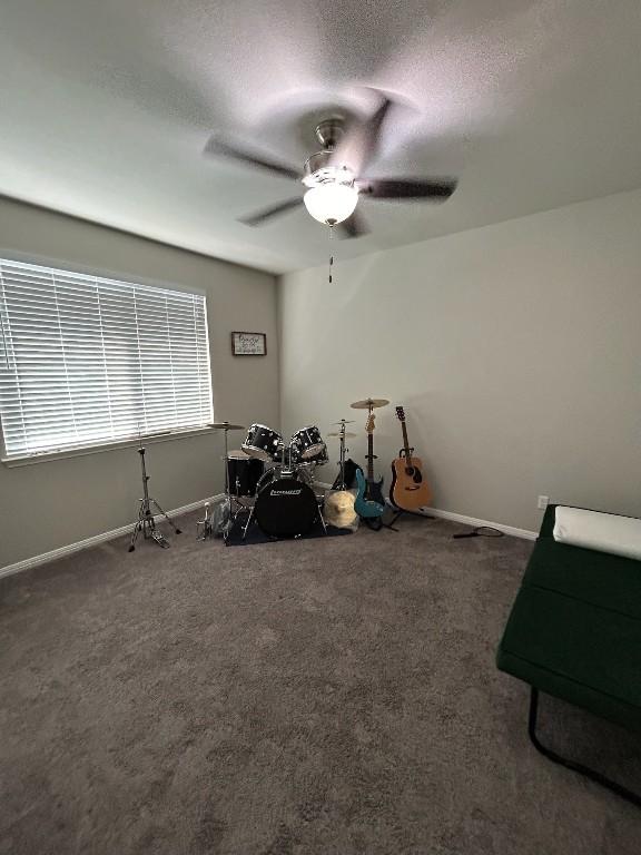 misc room featuring dark colored carpet, ceiling fan, a textured ceiling, and baseboards