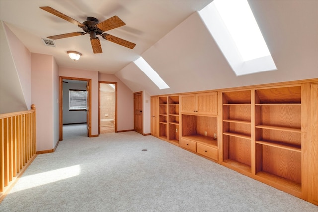 additional living space with ceiling fan, vaulted ceiling with skylight, and light carpet