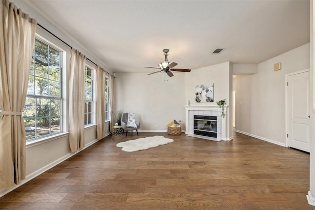 unfurnished room with dark hardwood / wood-style flooring, a tiled fireplace, and ceiling fan