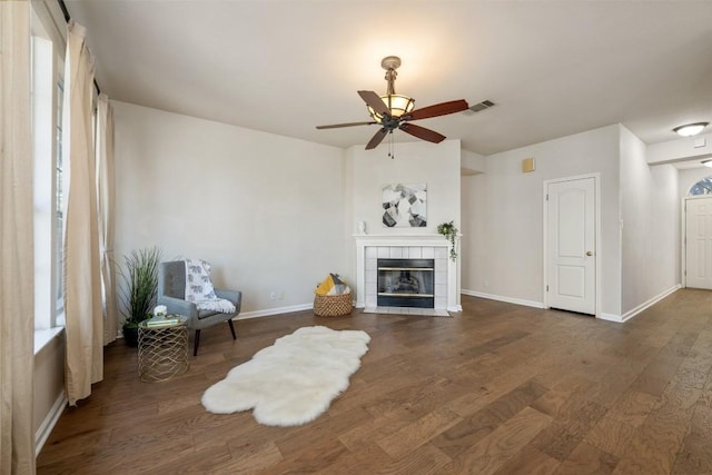 unfurnished living room featuring dark wood-type flooring, ceiling fan, plenty of natural light, and a tiled fireplace