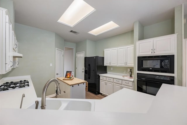 kitchen with butcher block counters, black appliances, a center island, and white cabinets