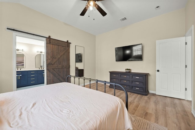 bedroom featuring ceiling fan, ensuite bathroom, a barn door, and light hardwood / wood-style flooring