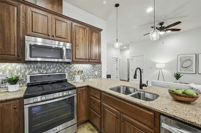 kitchen featuring sink, light stone counters, appliances with stainless steel finishes, pendant lighting, and backsplash