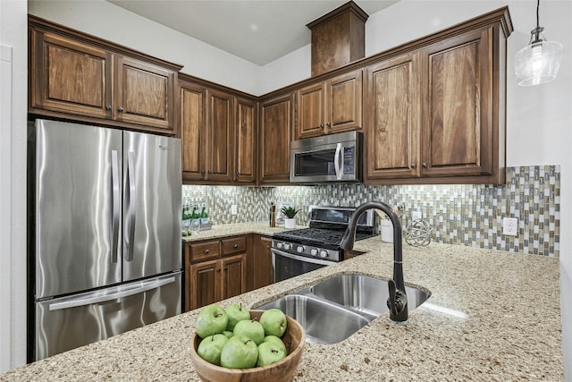 kitchen featuring tasteful backsplash, light stone counters, hanging light fixtures, stainless steel appliances, and a sink