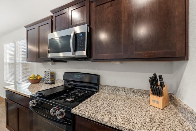 kitchen featuring stainless steel microwave, light stone countertops, black gas range oven, and dark brown cabinets