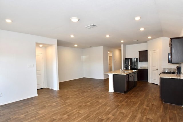 kitchen with black refrigerator, an island with sink, sink, range, and dark wood-type flooring