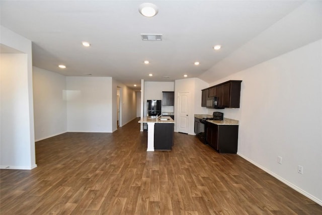 kitchen with sink, a kitchen island with sink, dark brown cabinetry, black appliances, and dark hardwood / wood-style flooring