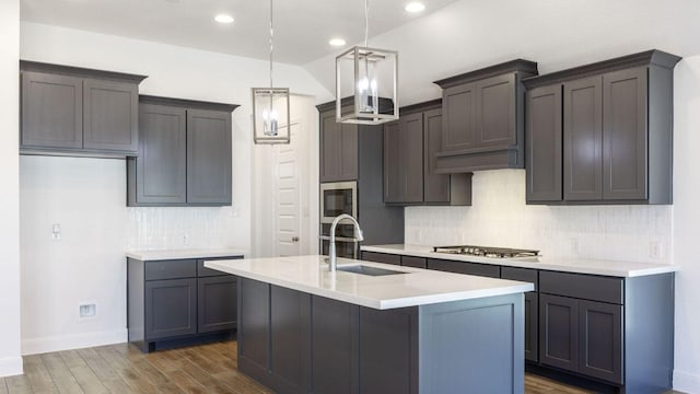 kitchen with an island with sink, dark wood-style flooring, stainless steel appliances, light countertops, and decorative light fixtures