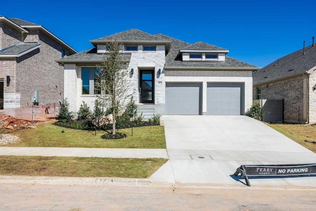 prairie-style home with brick siding, an attached garage, concrete driveway, and a front lawn