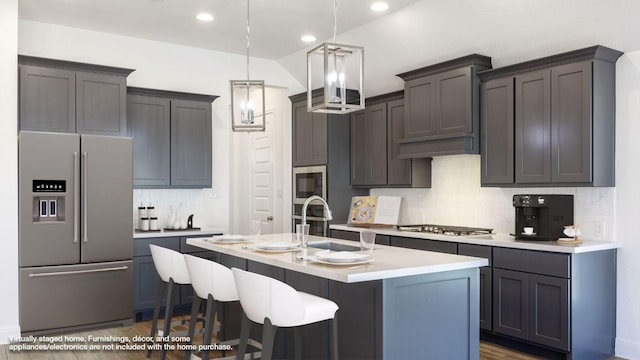 kitchen with pendant lighting, a kitchen island with sink, a sink, appliances with stainless steel finishes, and light countertops