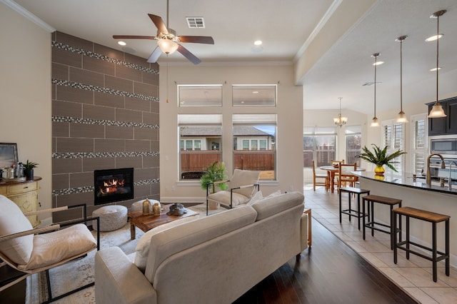 tiled living room with crown molding, sink, a fireplace, and ceiling fan with notable chandelier