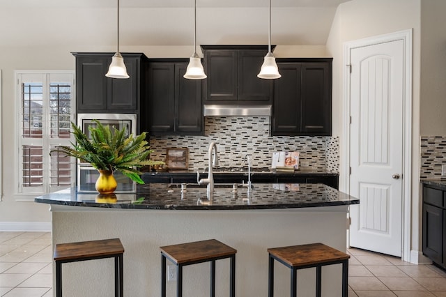 kitchen featuring pendant lighting, a breakfast bar area, backsplash, an island with sink, and light tile patterned flooring