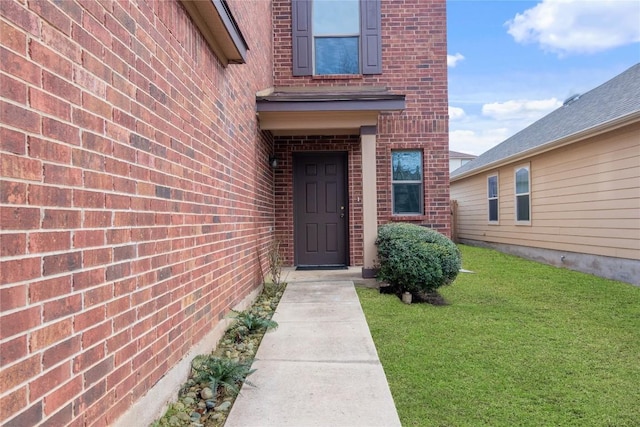 entrance to property with brick siding and a yard