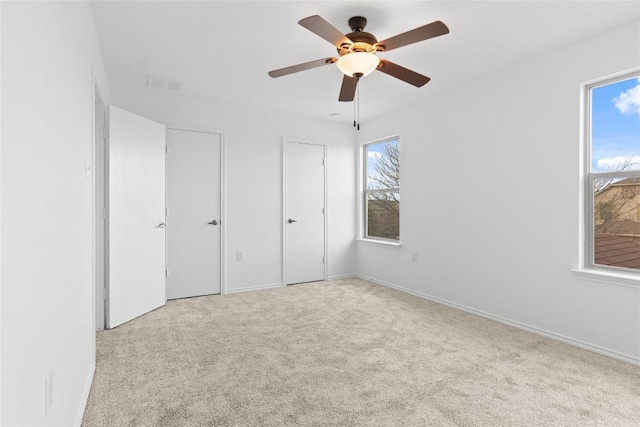 unfurnished bedroom featuring visible vents, two closets, a ceiling fan, carpet floors, and baseboards