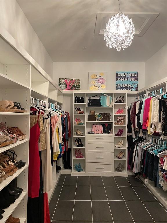 spacious closet with a notable chandelier and dark tile patterned floors