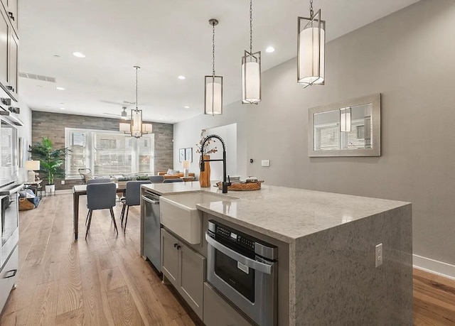 kitchen with sink, dishwasher, hanging light fixtures, an island with sink, and light wood-type flooring