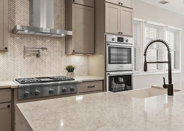 kitchen with appliances with stainless steel finishes, wall chimney exhaust hood, light stone countertops, and sink