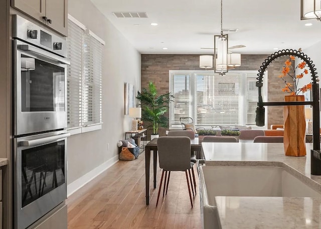 kitchen featuring sink, a chandelier, double oven, pendant lighting, and light hardwood / wood-style floors