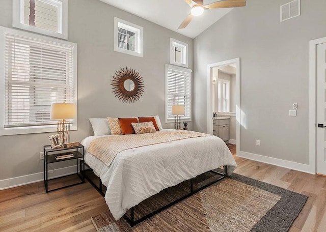 bedroom featuring multiple windows, ensuite bath, high vaulted ceiling, and light hardwood / wood-style flooring