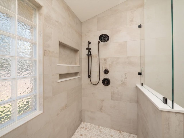 bathroom with a tile shower and lofted ceiling