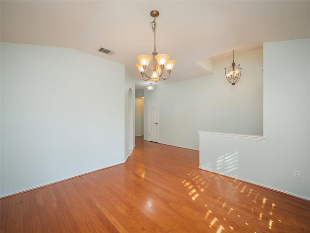 empty room featuring vaulted ceiling, a chandelier, and hardwood / wood-style floors