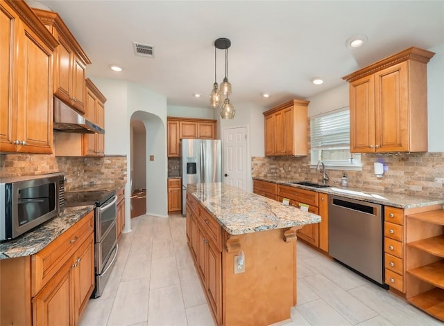 kitchen with sink, a kitchen island, pendant lighting, stainless steel appliances, and light stone countertops