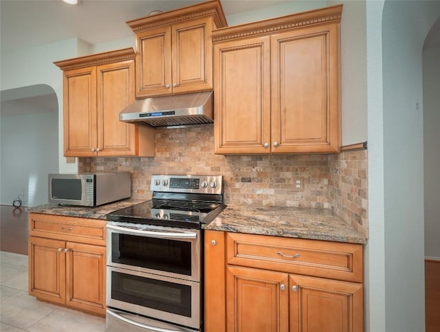 kitchen with light stone counters, stainless steel appliances, tasteful backsplash, and exhaust hood