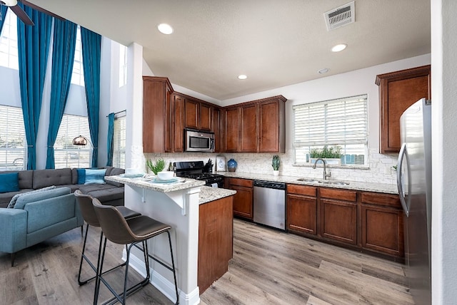 kitchen with sink, appliances with stainless steel finishes, a kitchen breakfast bar, light hardwood / wood-style floors, and decorative backsplash