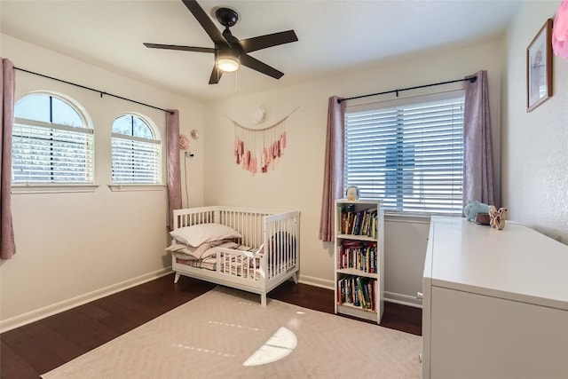 bedroom featuring a nursery area, ceiling fan, and dark hardwood / wood-style floors