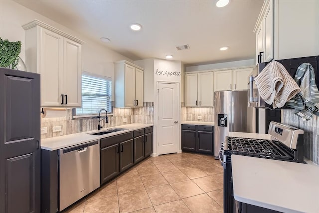 kitchen with appliances with stainless steel finishes, tasteful backsplash, sink, white cabinets, and light tile patterned floors