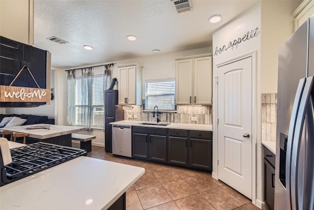 kitchen with sink, a textured ceiling, light tile patterned floors, appliances with stainless steel finishes, and decorative backsplash