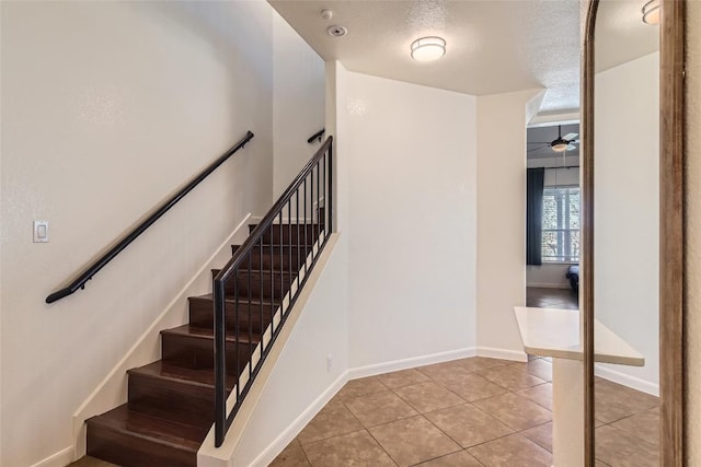 stairway with ceiling fan, tile patterned floors, and a textured ceiling