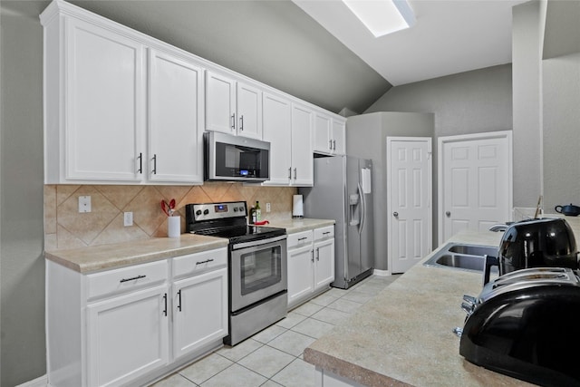 kitchen with vaulted ceiling, light tile patterned flooring, appliances with stainless steel finishes, white cabinets, and backsplash