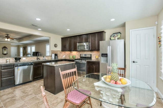 kitchen with appliances with stainless steel finishes, kitchen peninsula, decorative backsplash, light stone counters, and dark brown cabinetry