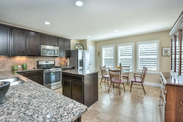 kitchen with a kitchen island, appliances with stainless steel finishes, decorative backsplash, dark brown cabinetry, and light stone countertops