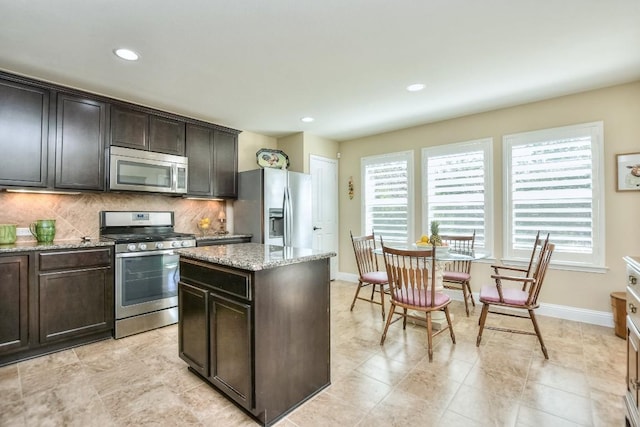 kitchen featuring backsplash, a center island, light stone counters, stainless steel appliances, and dark brown cabinets