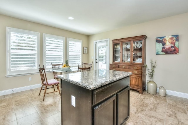 kitchen with dark brown cabinetry, light stone countertops, a center island, and light tile patterned flooring